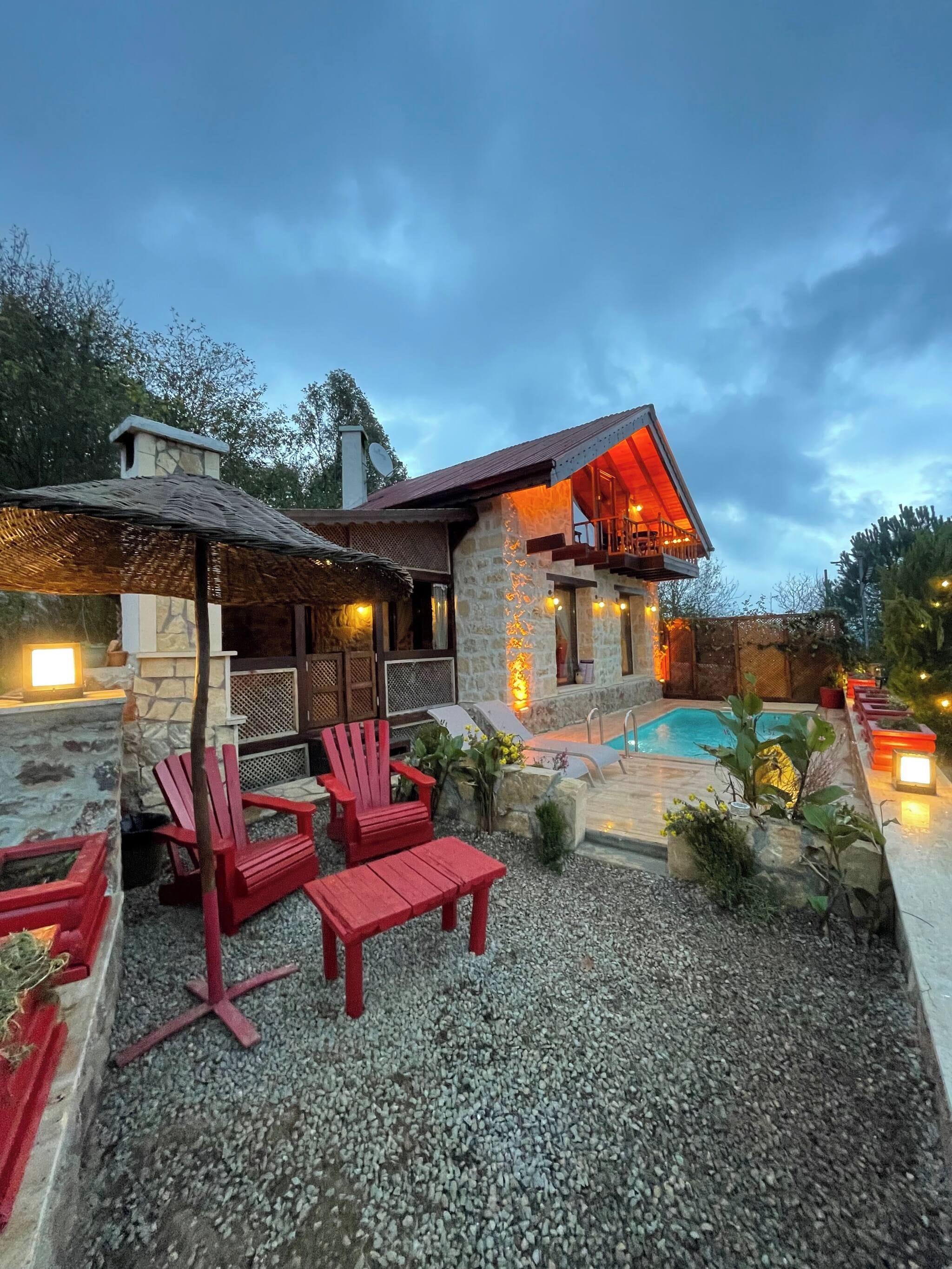 Ein Steinhaus mit Pool, roten Adirondack-Stühlen und einer überdachten Terrasse.