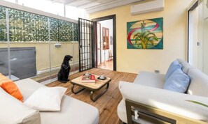 Een moderne woonkamer met een glazen deur naar een balkon, een witte bank, een kleine tafel met een boek en een beerbeeld.