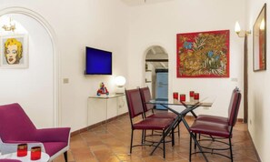 Een eetgedeelte met een glazen tafel, rode stoelen, een blauwe tv aan de muur en een rood schilderij.