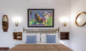 Un dormitorio con una cama, dos mesitas de noche, una obra de arte en la pared y un espejo redondo.