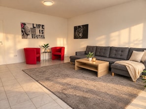Un salon moderne avec un canapé gris, des fauteuils rouges, une table basse et un tapis.