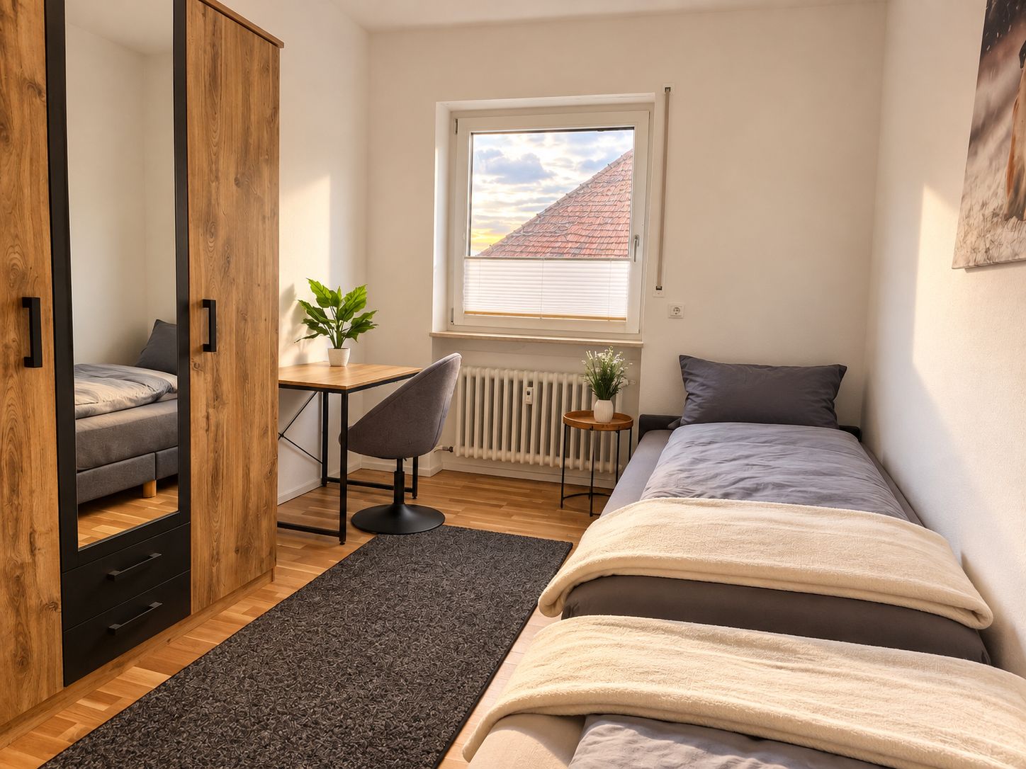 A bedroom with a bed, a desk with a chair, a window with a view of a building, and a radiator.