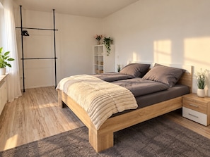 Une chambre à coucher moderne avec un lit en bois, une table de chevet, une commode, une armoire et une plante.