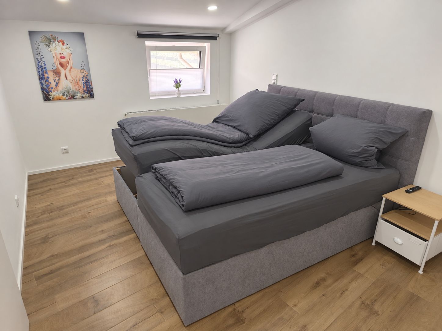 Een moderne slaapkamer met een groot bed, een nachtkastje en een raam met jaloezieën.