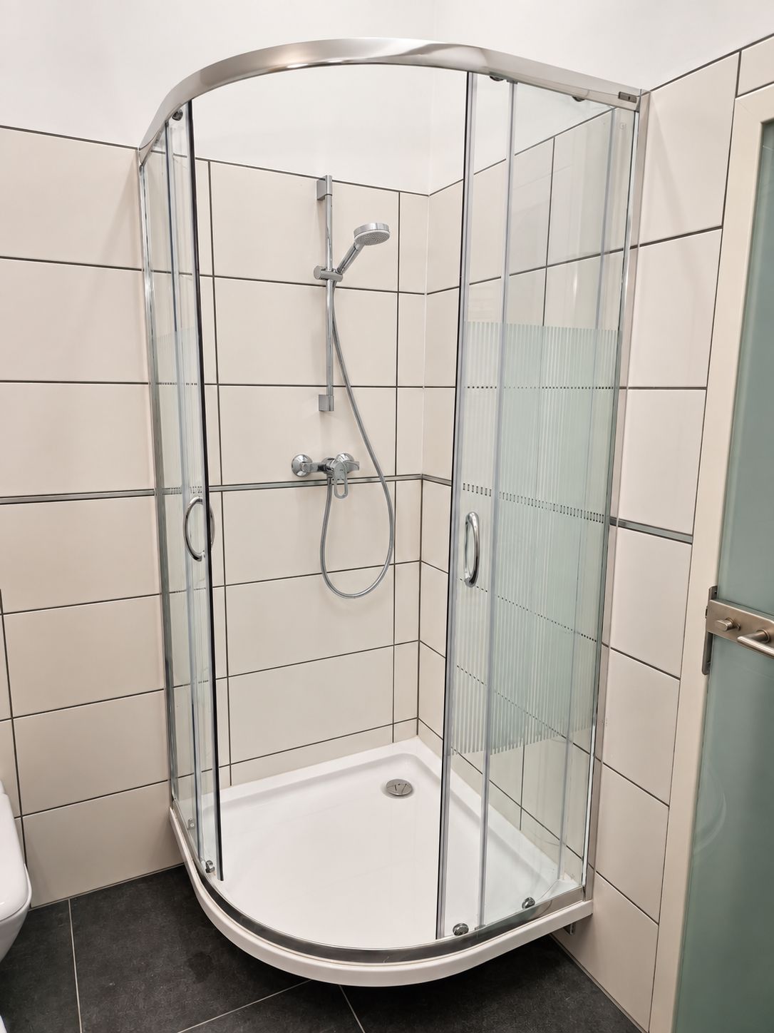 Eine Duschkabine mit Glaswänden, einer Handbrause und einem am Wand montierten Wasserhahn.