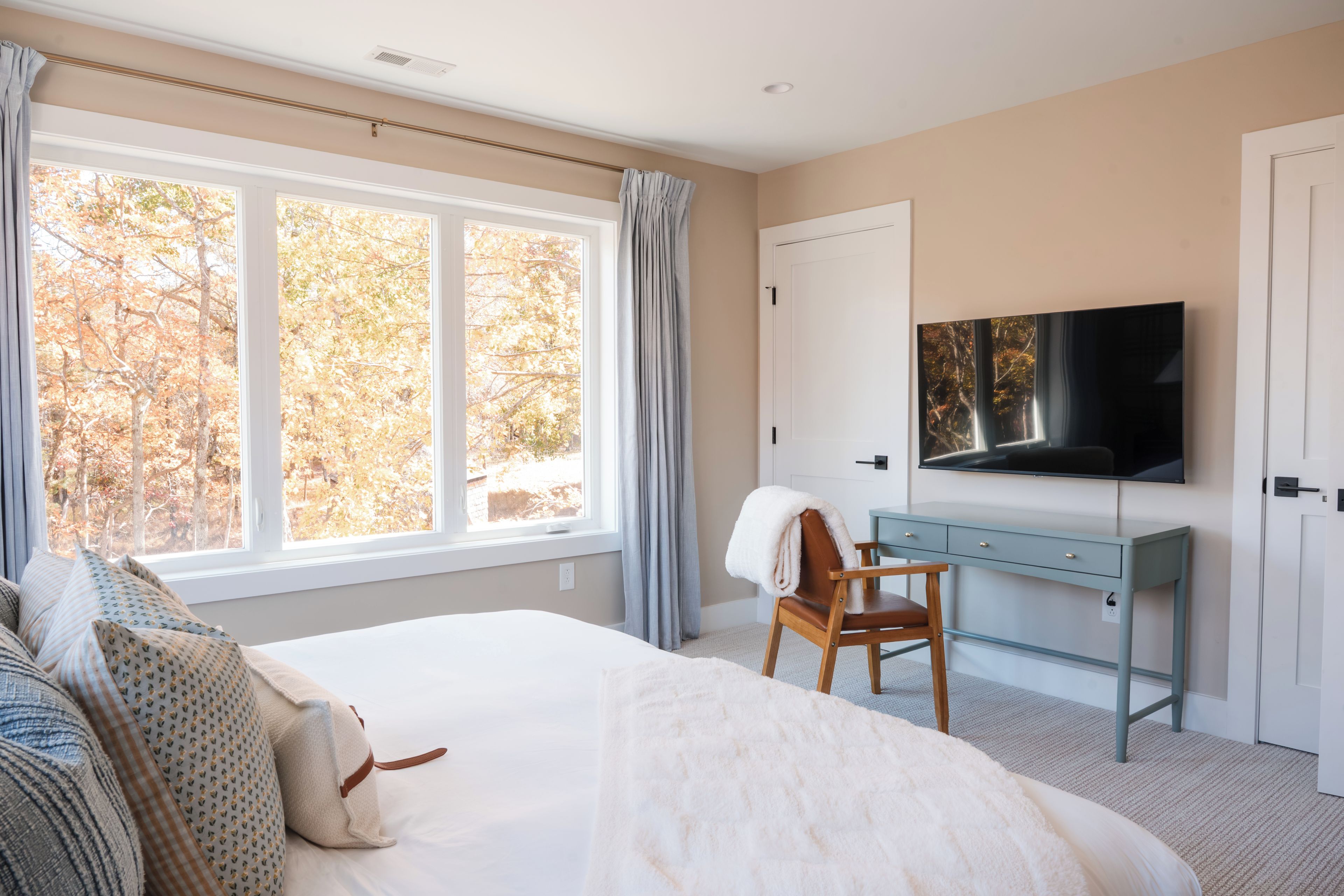 A bedroom with a large bed, a desk, a chair, a television, and a window with curtains.