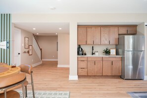 A modern kitchen with wooden cabinets, a stainless steel refrigerator, and a dining area with a table and chairs. - NEW Luxe 6BR | Speakeasy, Cinema, Hidden Playroom (Albrightsville)