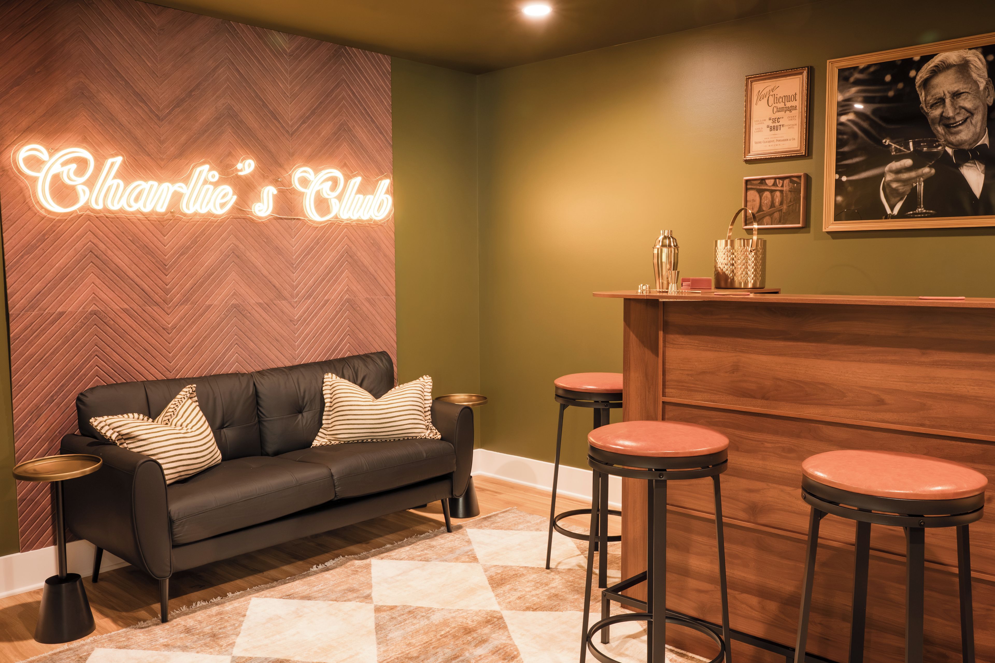 A bar area with a neon sign, a sofa, and bar stools.
