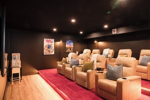 A cinema room with reclining seats, posters on the wall, and a red carpet. - NEW Luxe 6BR | Speakeasy, Cinema, Hidden Playroom (Albrightsville)