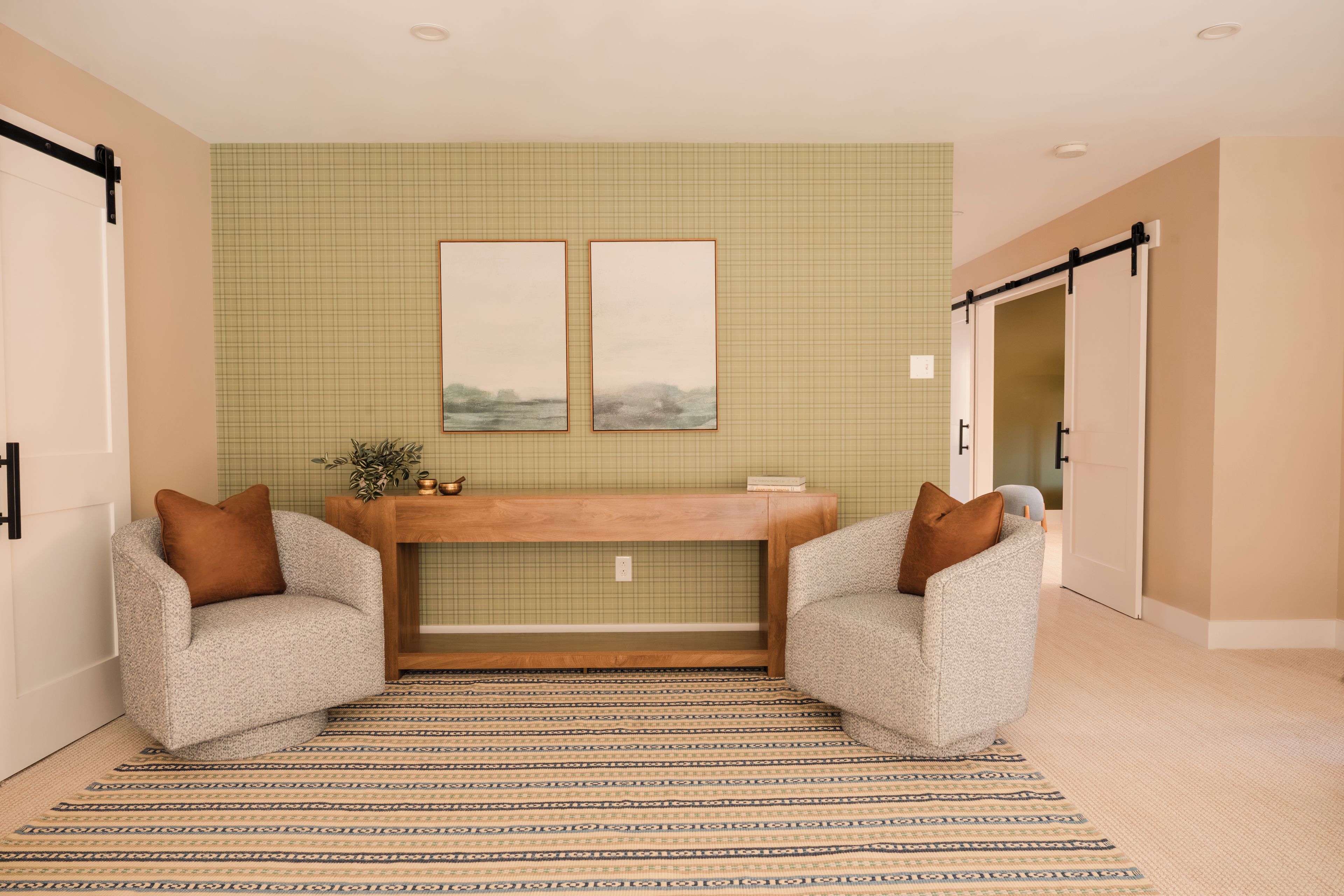 A room with a wooden console table, two armchairs, a patterned rug, and a green checkered wall.