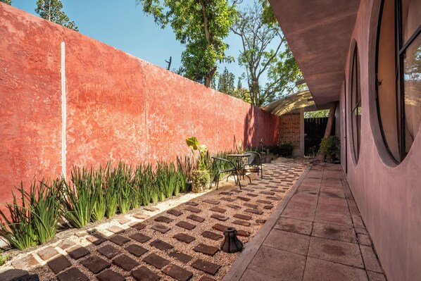 A patio area with a red wall, a brick pathway, and a table with chairs.