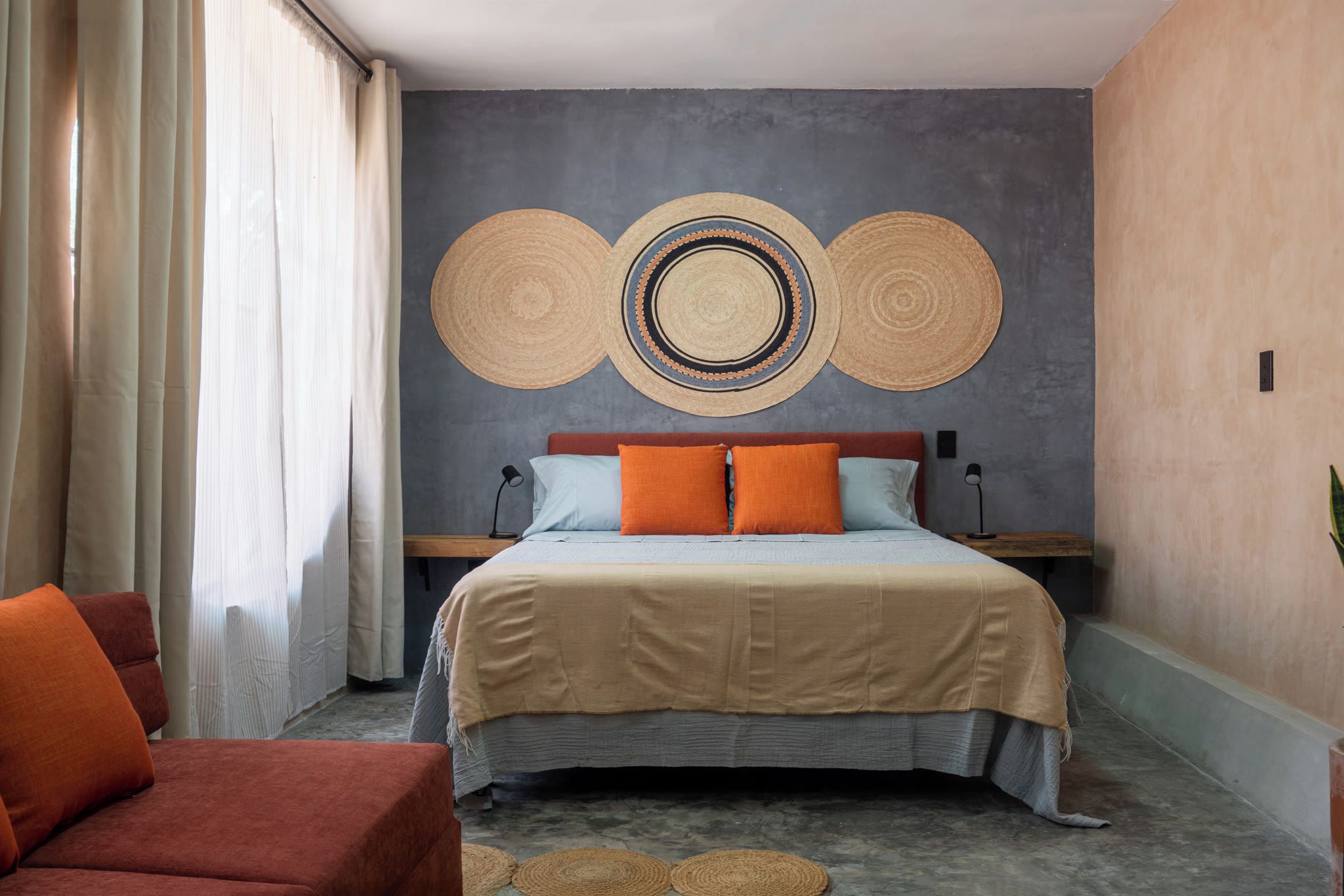 Una camera d'albergo con un letto, due comodini, una poltrona e un grande elemento decorativo a parete.