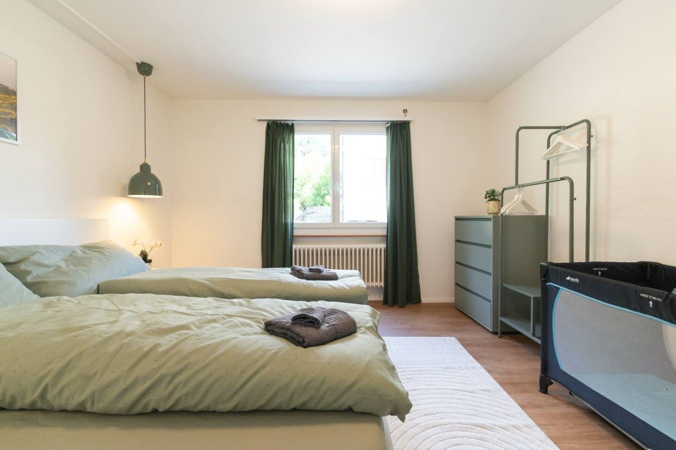 Ein Schlafzimmer mit zwei Betten, einem Schminktisch, einem Heizkörper und einem Fenster mit Vorhängen.