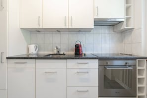 Een moderne keuken met witte kasten, een zwart aanrecht, een koffiezetapparaat, een waterkoker en een inbouwoven.