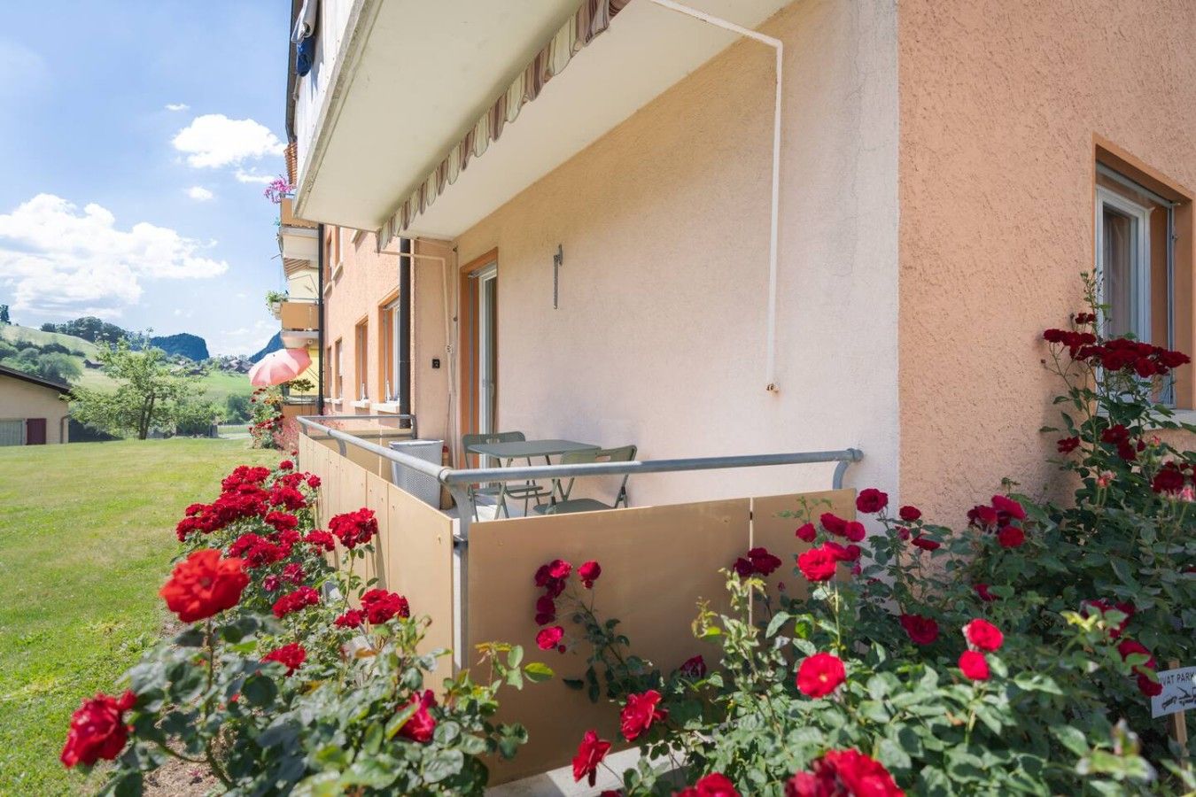Een hotel met een balkon, terras en een tuin met rode bloemen.
