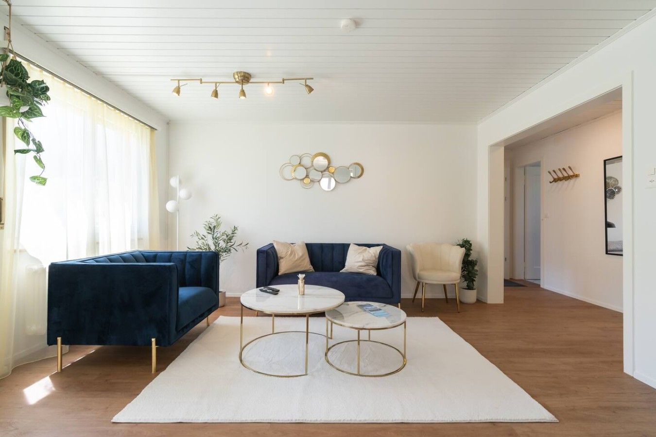 Een moderne woonkamer met een blauwe bank, twee ronde salontafels en een decoratief wandobject.