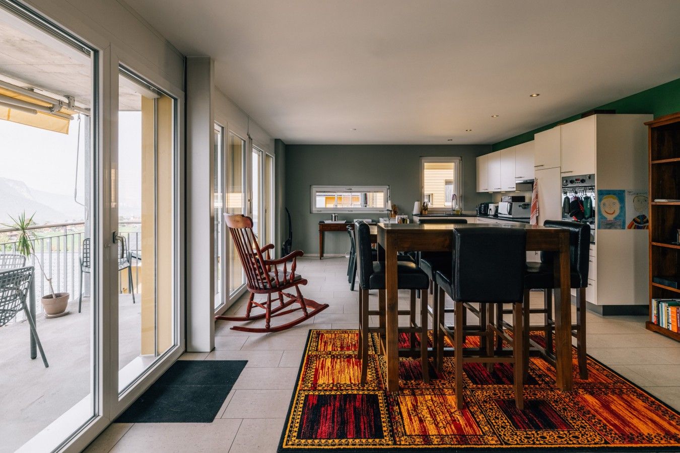 Una cocina moderna con armarios blancos, una zona de comedor con una mesa y sillas de madera, y un amplio ventanal con vistas a un balc ón.