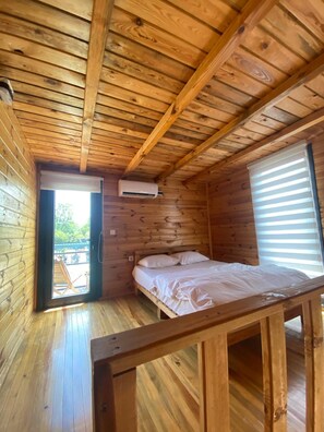 Ein Zimmer in einer Holzhütte mit einem Bett, einer Klimaanlage und einem Fenster mit Jalousien.