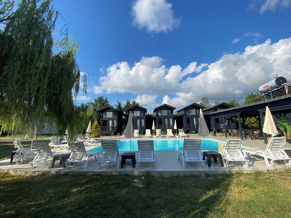 A pool area with lounge chairs and umbrellas, surrounded by wooden cabins with large windows. - Agva Riverside Bungalow (Şile)