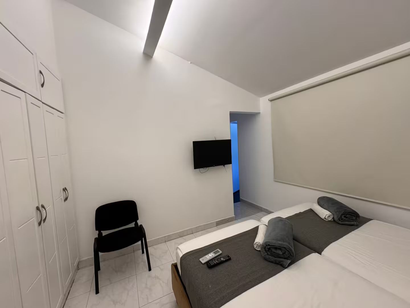 A hotel room with a bed, a chair, a TV mounted on the wall, and a wardrobe.