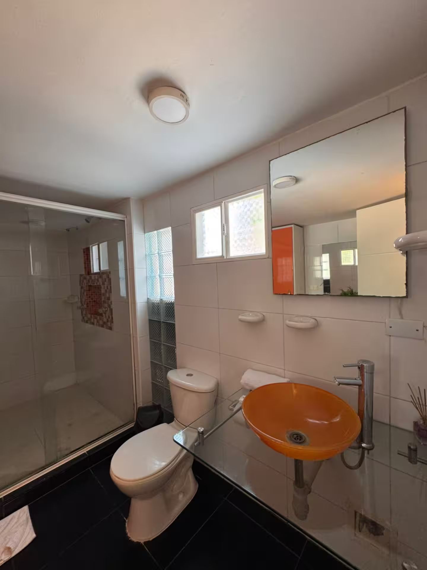 A bathroom with a glass shower enclosure, a white toilet, and an orange sink.