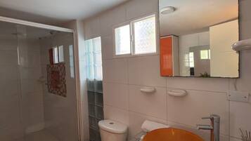 A bathroom with a glass shower enclosure, a white toilet, and an orange sink.
