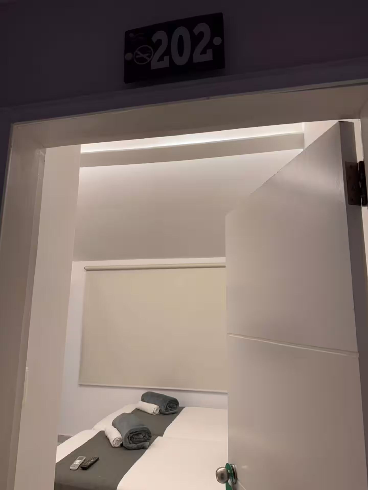 Une chambre d’hôtel avec un lit, une table de chevet et un panneau fixé au mur indiquant le numéro de chambre : 202.