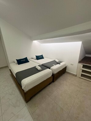 Quarto de hotel com duas camas, uma escrivaninha e uma pequena cozinha compacta.