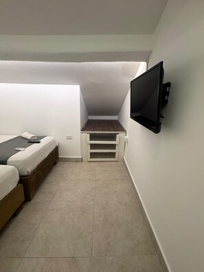 Een kleine, compacte kamer met een bed, een bureau en een aan de muur bevestigde televisie.