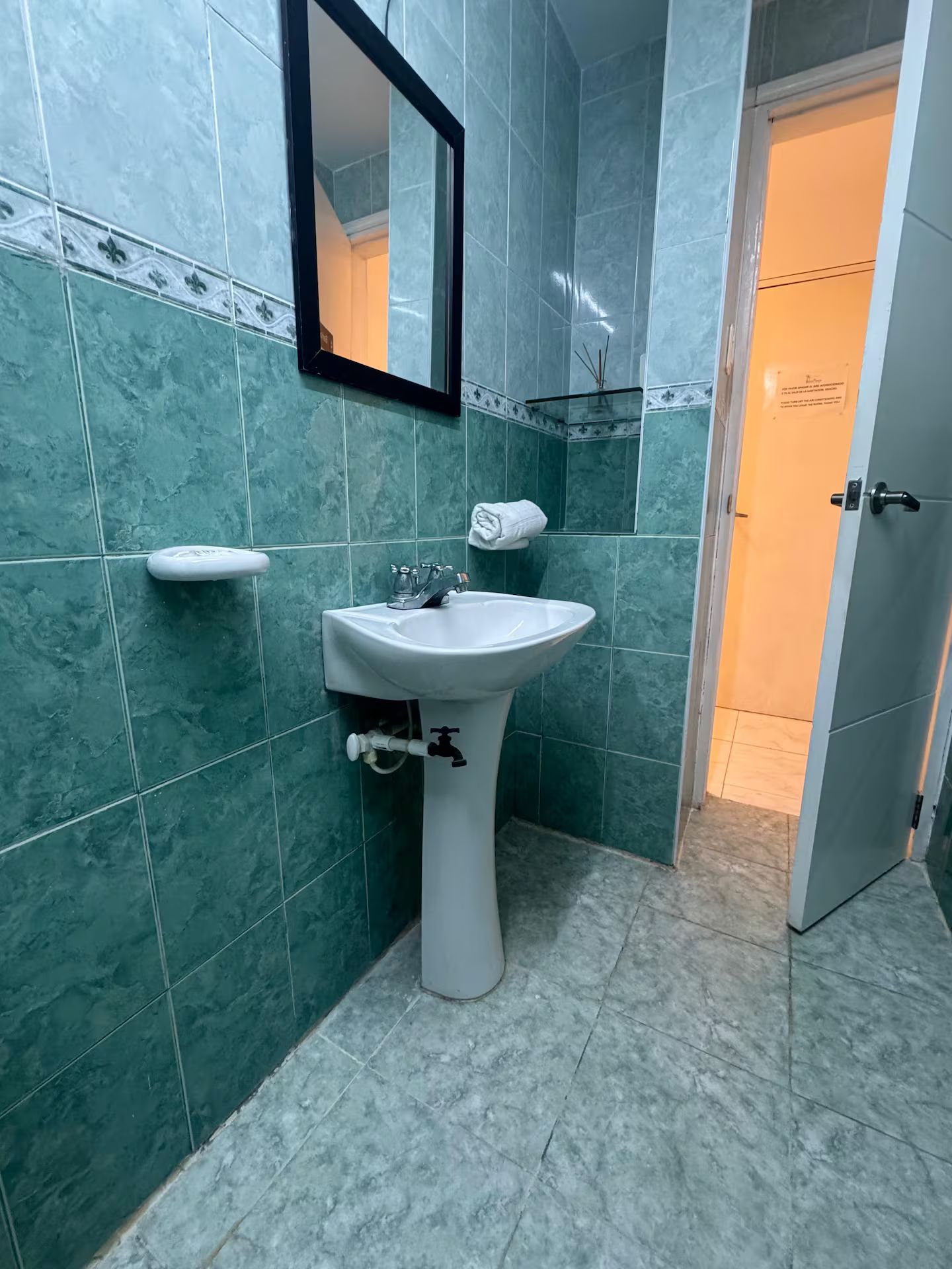 Een badkamer met een witte wastafel, een spiegel en groene tegels.