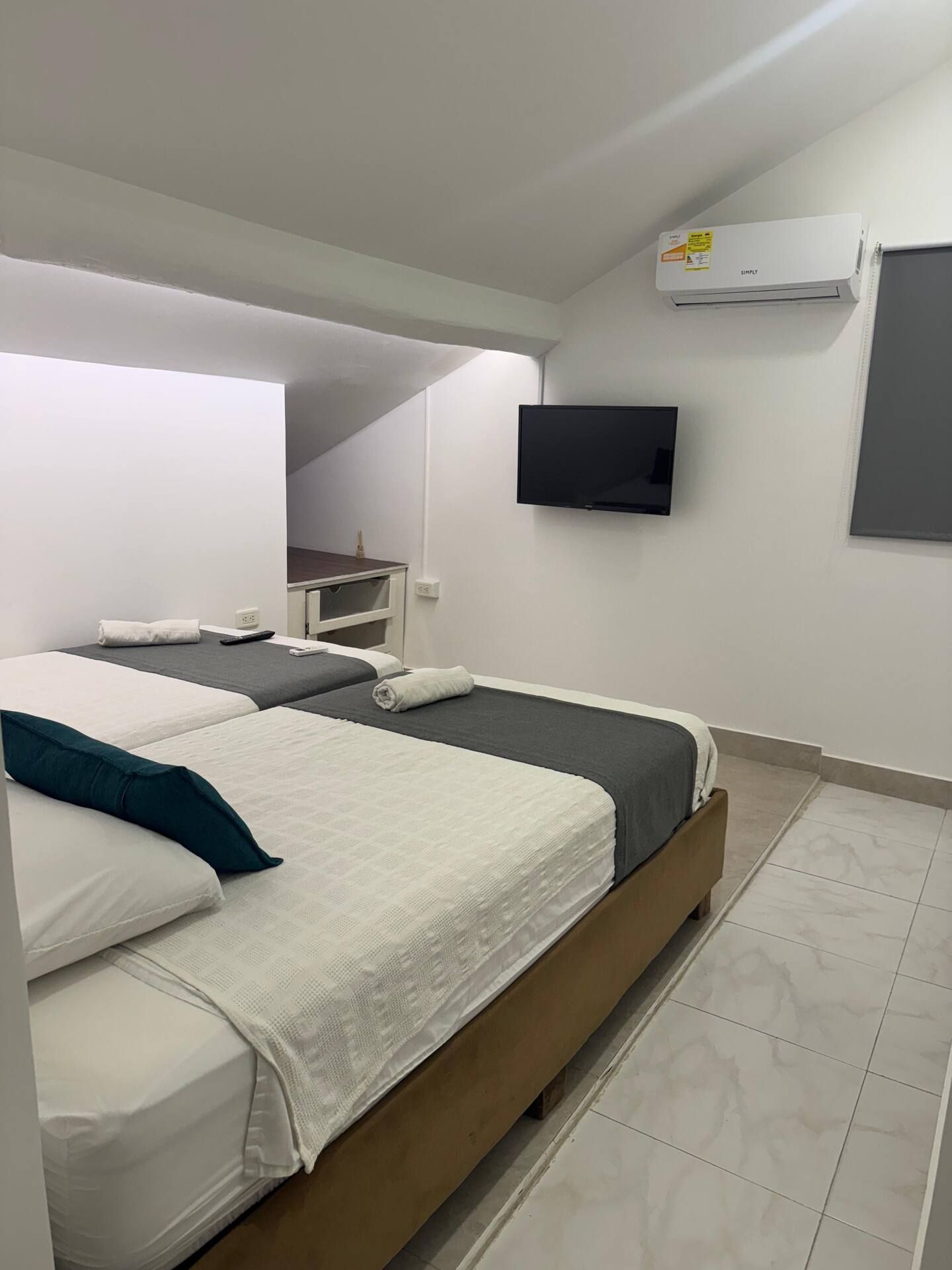 Habitación de hotel con dos camas, un televisor de pantalla plana montado en la pared y un equipo de aire acondicionado.