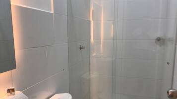 Casa de banho com cabine de chuveiro em vidro, pia branca e duas sanitas.