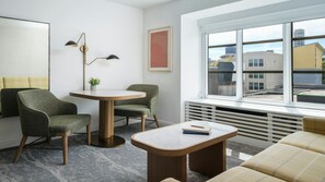 Una sala de estar moderna con una mesa redonda, dos sillones, un sofá, una lámpara de pie y un ventanal con vistas a la ciudad.