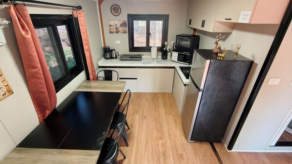 A compact kitchen with a dining table, a refrigerator, a microwave, and a coffee maker.