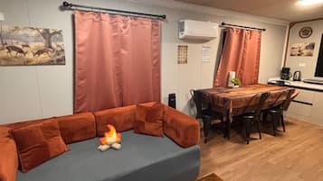 A living area with a sofa, a coffee table, a dining table with chairs, and an air conditioning unit.