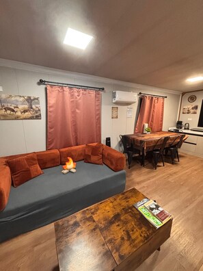 A living area with a sofa, a coffee table, a dining table with chairs, and an air conditioning unit.