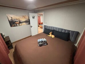 A bedroom with a bed, a painting of a deer, and a door leading to another room.
