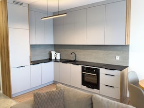 A modern kitchen with white cabinets, a black countertop, a built-in oven, and a coffee maker.