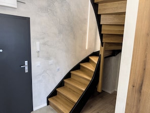A modern staircase with wooden steps and black railings, leading to a room with a textured wall and a door with a light switch.