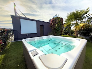 A hot tub in a backyard with a projector screen and a garden.