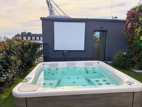 A hot tub with a control panel, a power outlet, and a window on a modern building.