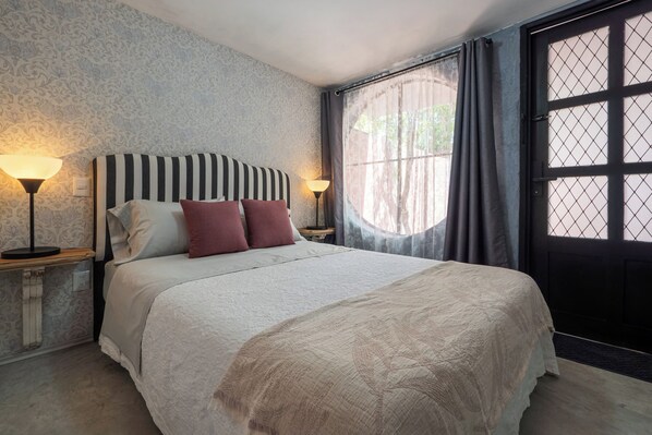 Een slaapkamer met een groot bed, twee bedlampen, een raam met gordijnen en behang met een patroon.