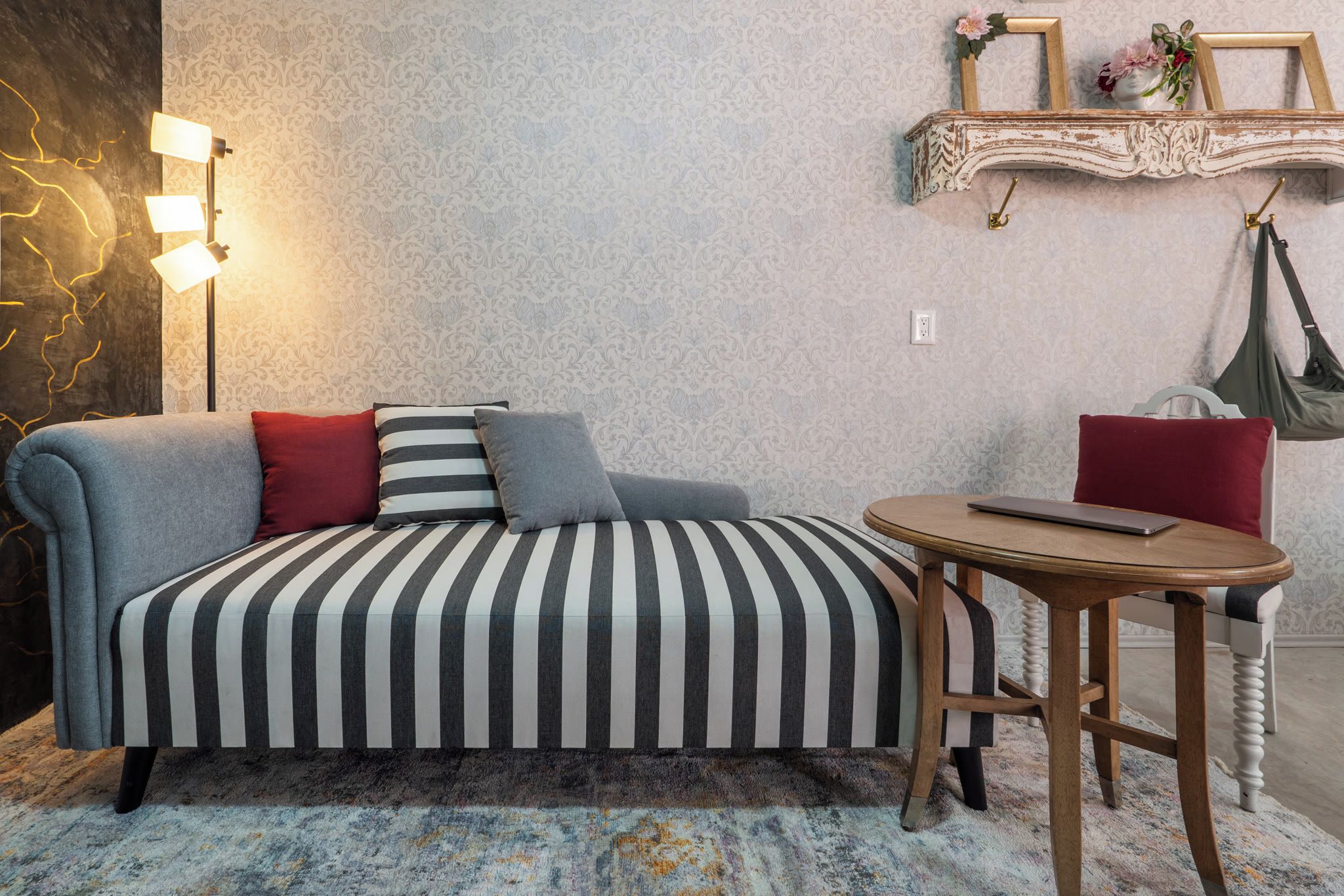 Un divano con cuscini a righe, un tavolo rotondo in legno e una mensola a parete con oggetti decorativi.