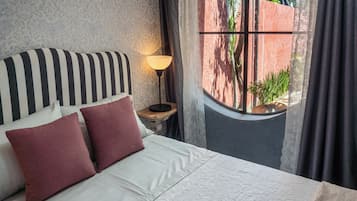 Ein Bett mit gestreifter Kopfteile, zwei Kissen, eine Nachttischlampe und ein Fenster mit Vorhängen.
