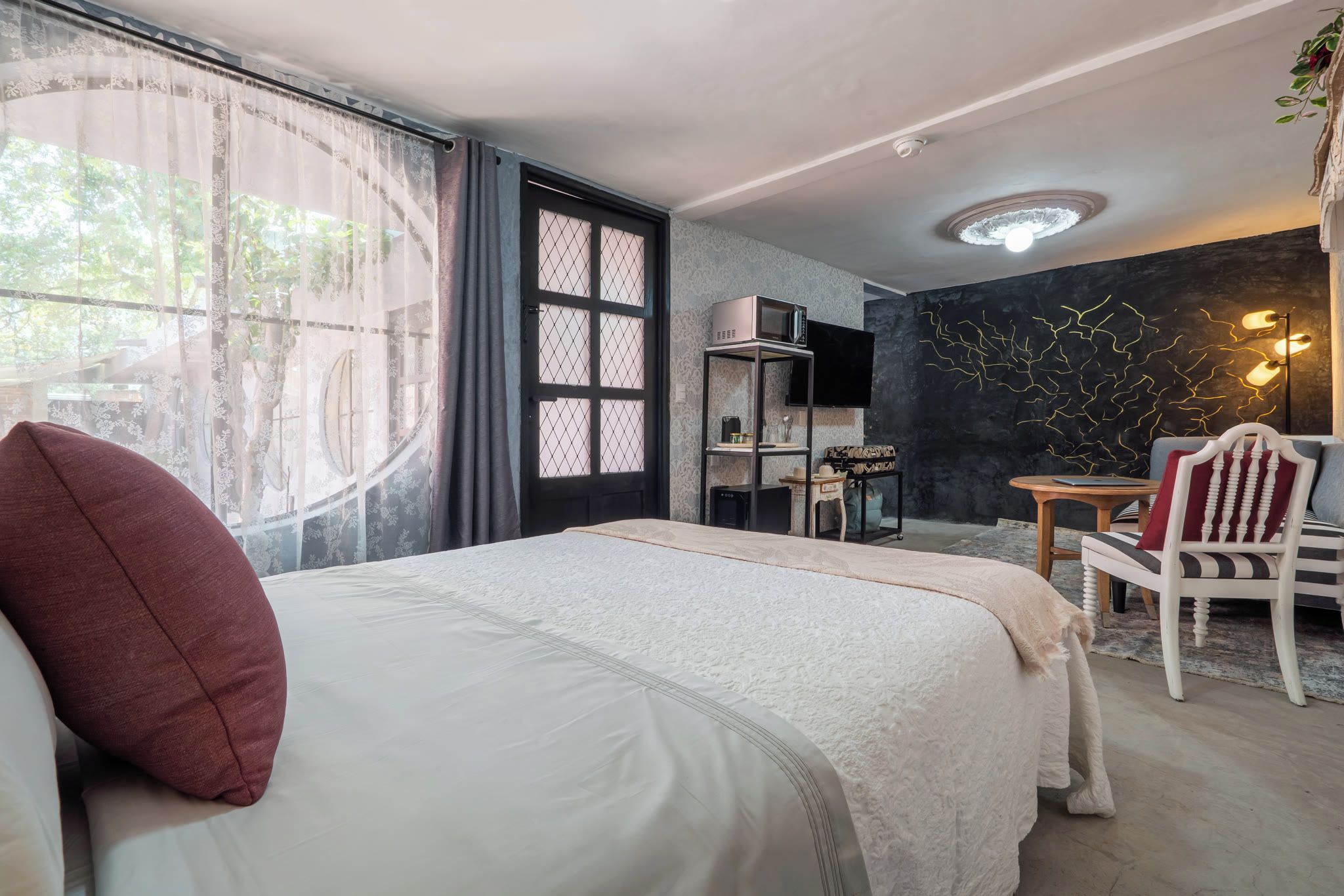 Una camera d'albergo con un letto, una scrivania, una sedia, un televisore e una parete con un lampadario originale.