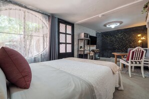 Habitación de hotel con cama, escritorio, silla, televisor y una pared con una lámpara original.