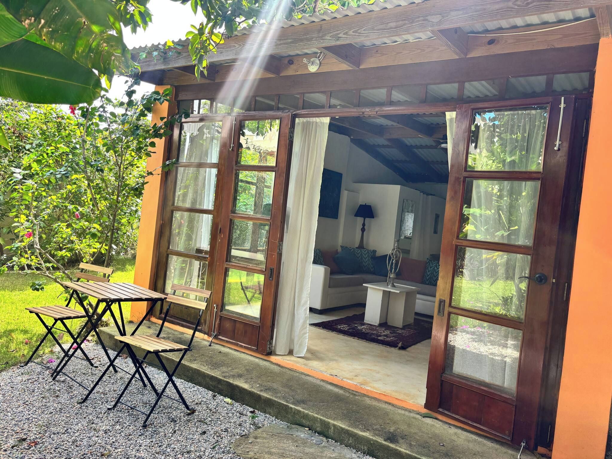 Une structure en bois dotée d’un porche abrité, d’un coin repas avec une table et des chaises, et offrant une vue sur un jardin.