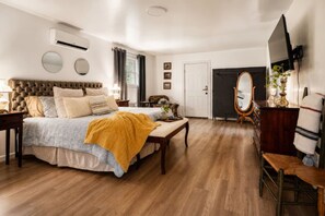 Un dormitorio con una cama grande, mesitas de noche, un tocador, un espejo y un televisor.