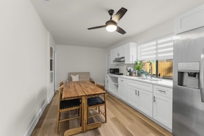 A modern kitchen with white cabinets, a wooden dining table, and a ceiling fan.