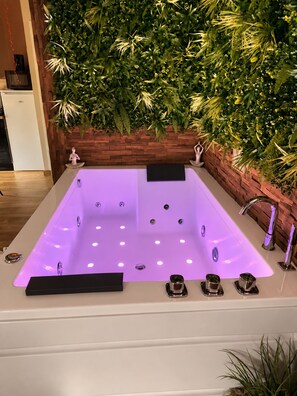 Ein modernes Badezimmer mit einer rechteckigen Badewanne, einer Holzvertäfelung mit Grünpflanzen und einem weißen Waschbecken mit Armatur.